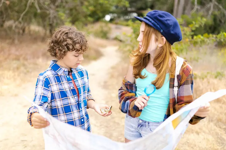 Dos niños explorando la naturaleza con un mapa y una brújula